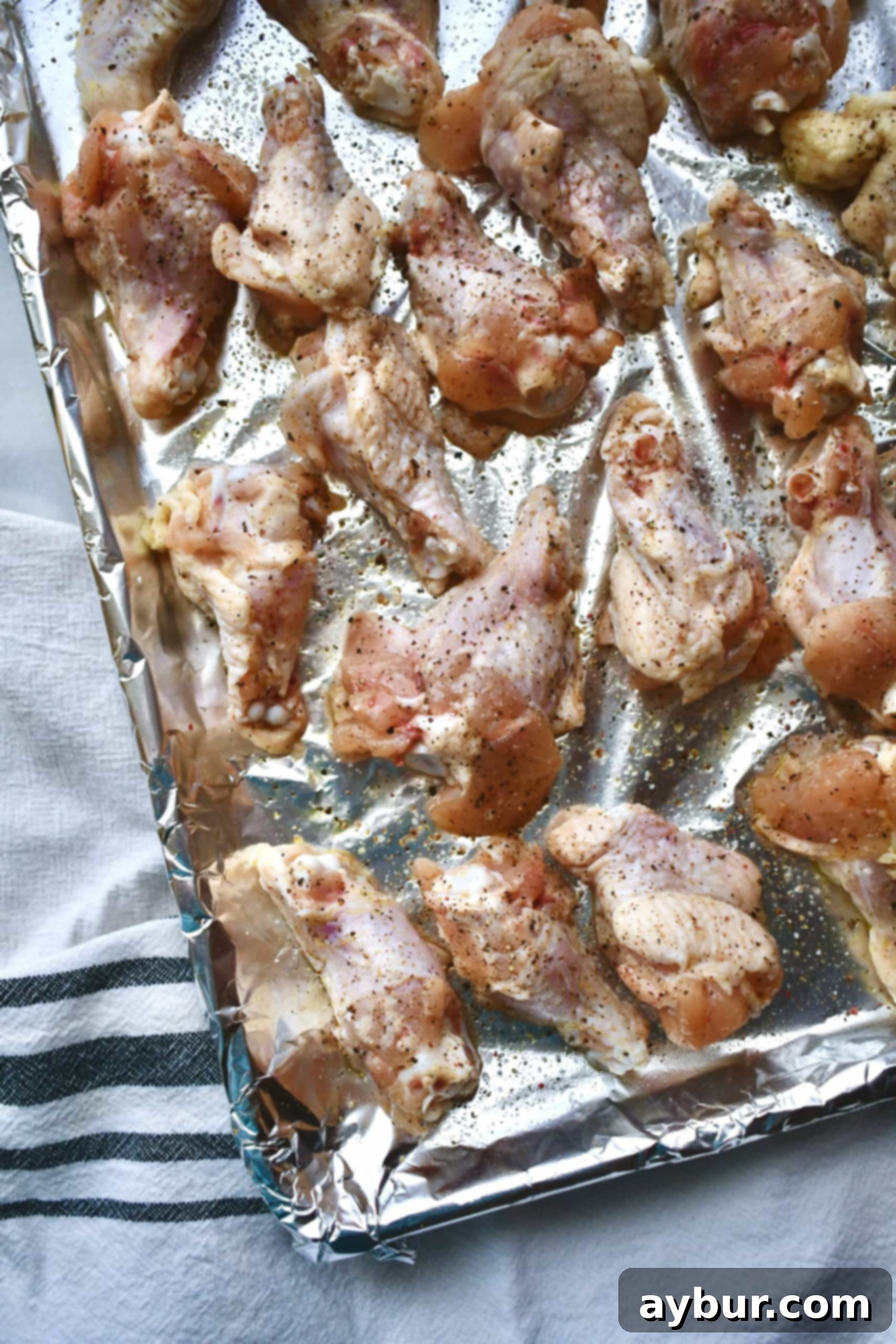 Perfectly dried and seasoned chicken wings arranged in a single layer on a foil-lined baking tray, ready for the oven.