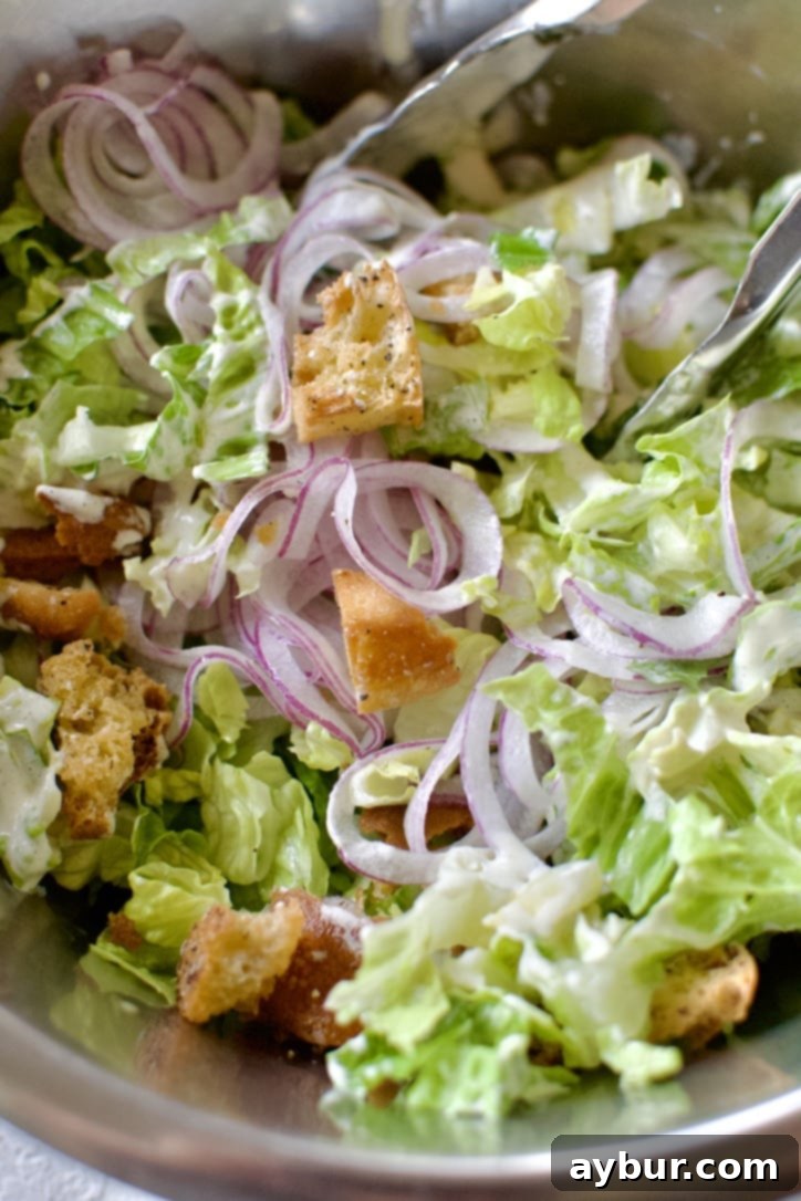 Traditional Caesar Salad 7 A large mixing bowl filled with crisp romaine lettuce, thinly sliced red onion, homemade croutons, and a creamy Caesar dressing, all tossed together to create a perfect Classic Caesar Salad.