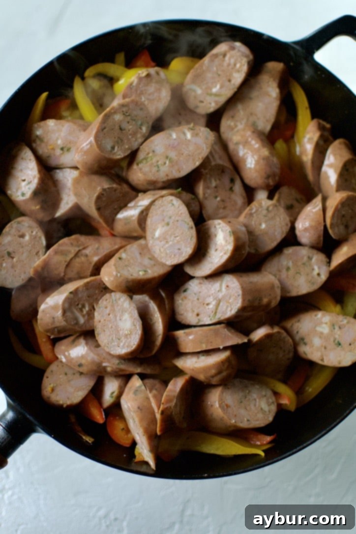 Sliced Italian sausage being added to a skillet with sautéed onions and peppers, ready to be cooked further and combined.