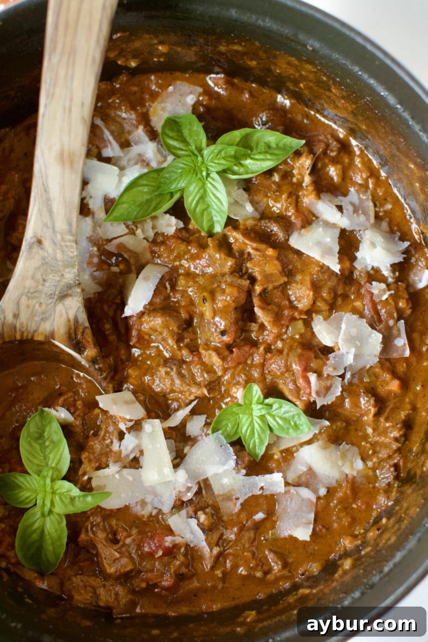 Finished Short Rib Bolognese sauce in a pot, ready to be served over pasta or polenta, garnished with fresh basil.