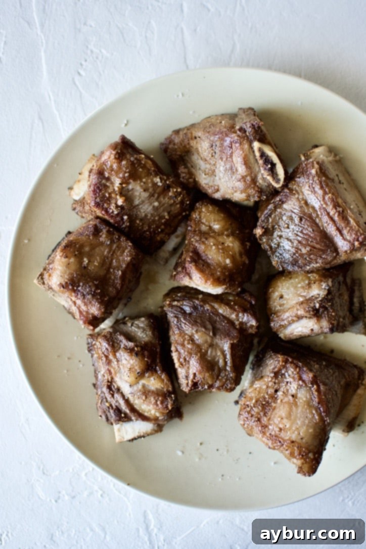 Perfectly seared Short Ribs resting on a plate after being browned on all sides, ready for the next step.