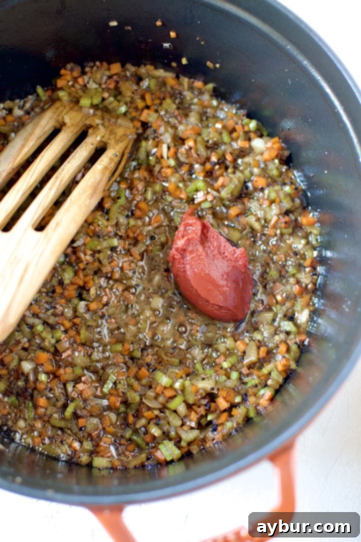 Cooked mirepoix and tomato paste in the bottom of a pan, ready for deglazing with wine.