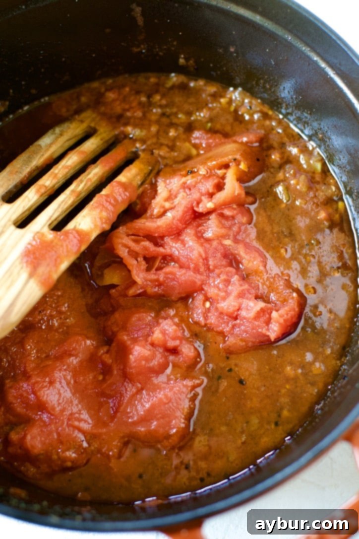 Hand-crushed San Marzano tomatoes being added to the pot with the simmering sauce base.