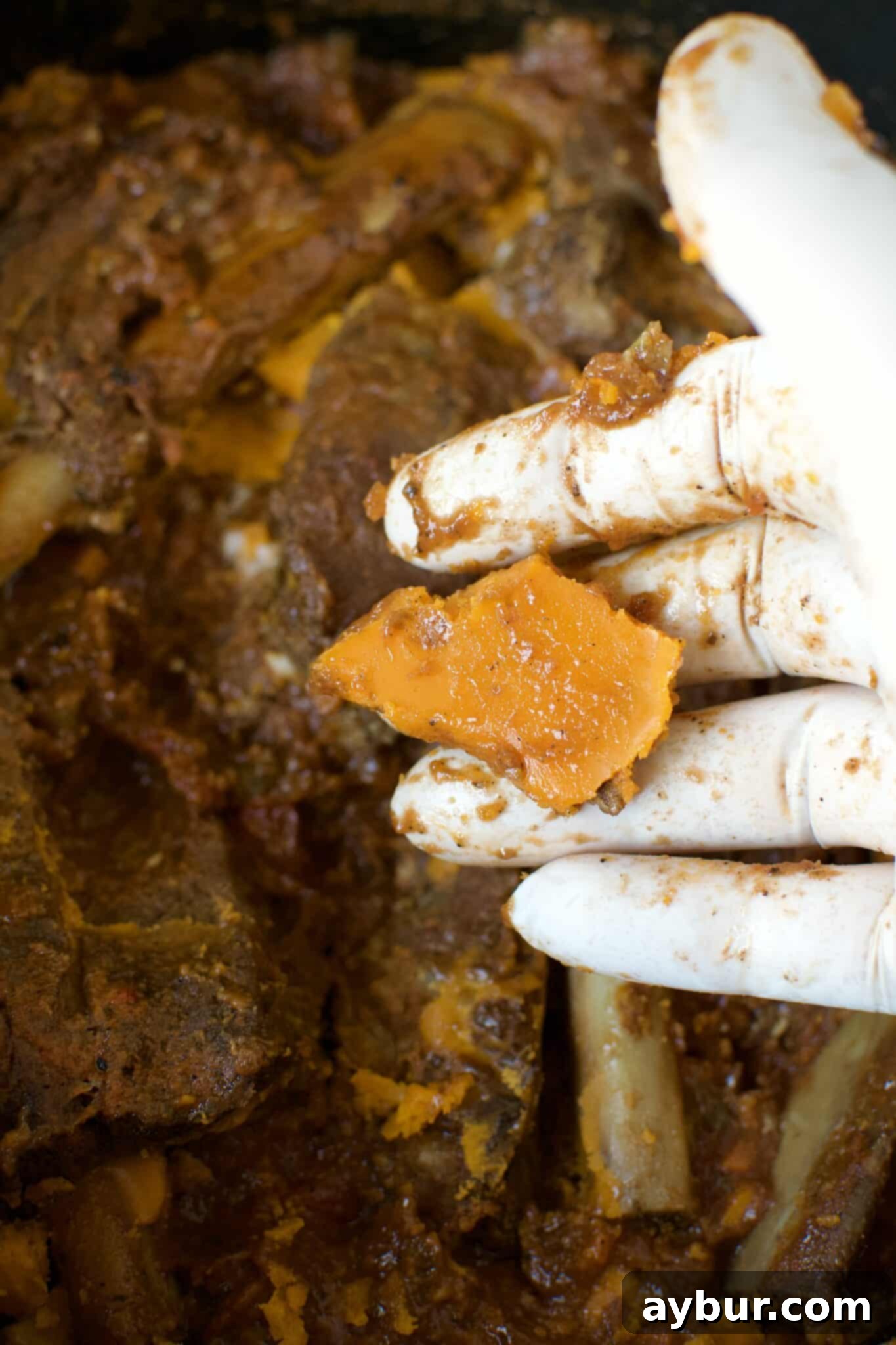 Hands removing the solidified fat layer from the top of the cooled short rib bolognese sauce.