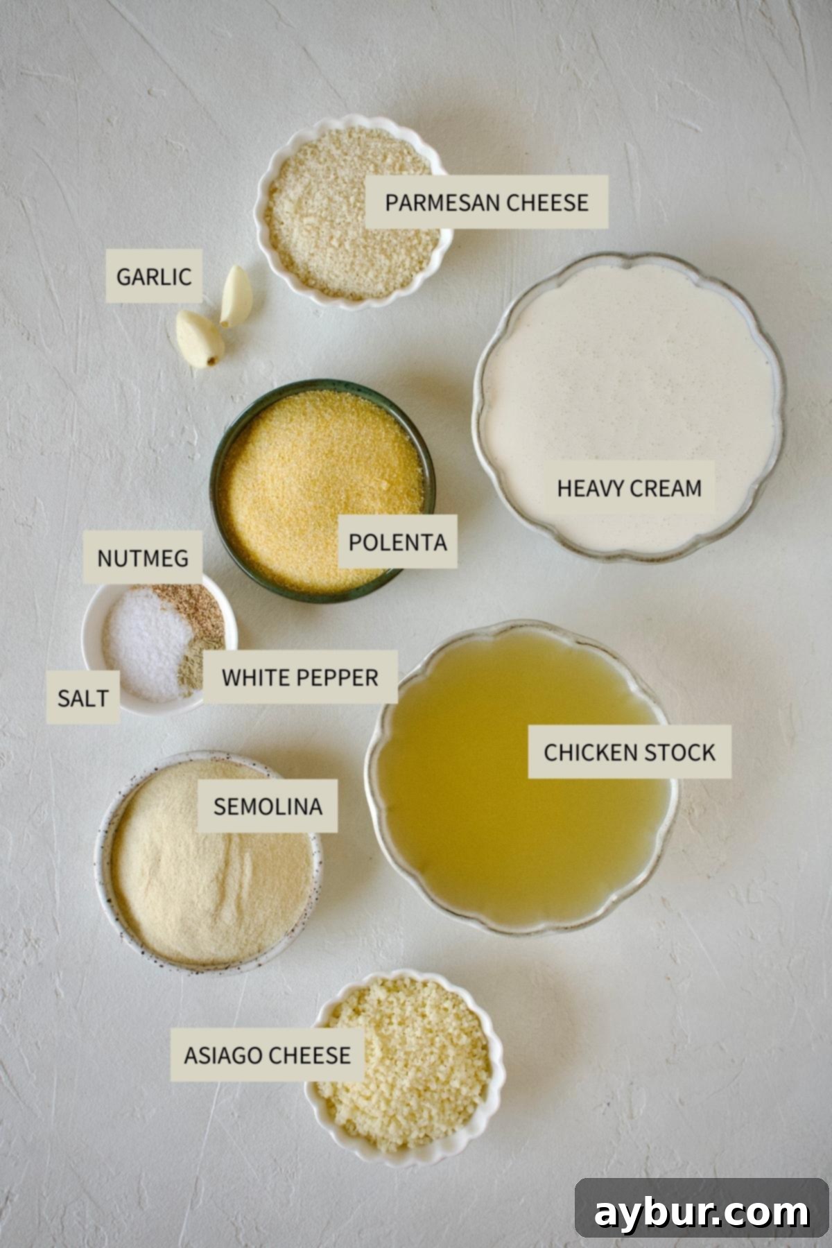 Velvety Creamy Polenta 3 All ingredients laid out for creamy polenta recipe: chicken stock, heavy cream, garlic, nutmeg, salt, white pepper, polenta, semolina, asiago, and parmesan cheese.