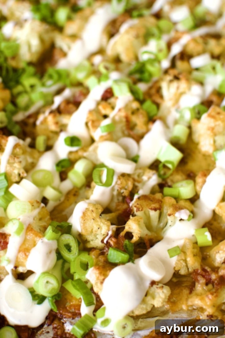 Another view of Loaded Baked Cauliflower on a sheet pan after cooking, with melted cheese and green onions.