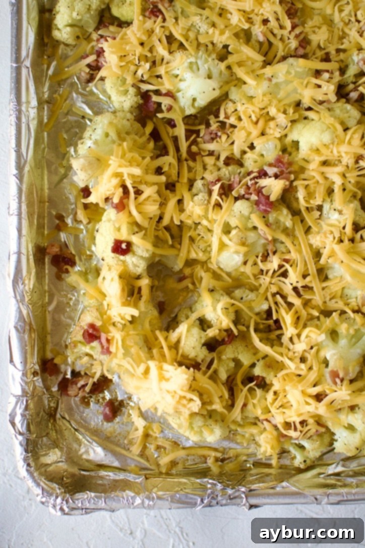 Roasted cauliflower with bacon bits and shredded cheddar cheese added, ready for broiling.
