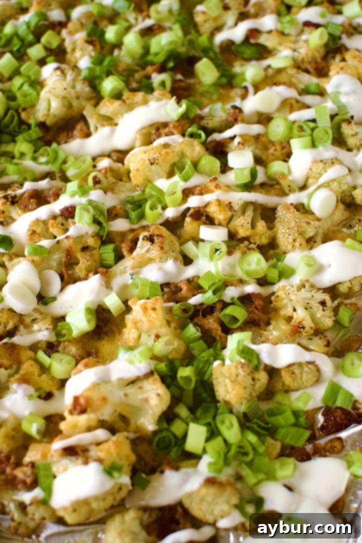 Loaded Baked Cauliflower on a sheet pan after cooking, garnished with green onions and ranch, ready to eat.