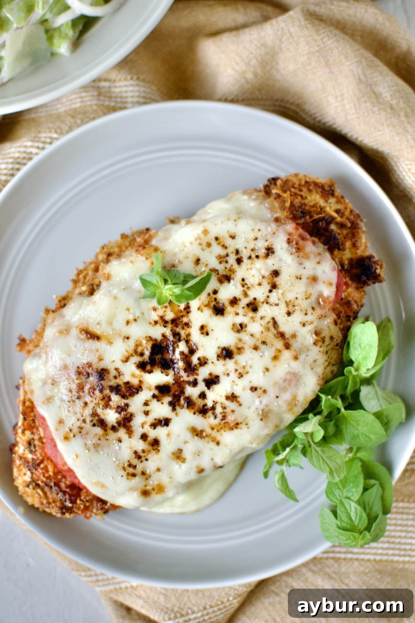 A close-up of a portion of baked chicken parmesan with a fork, showing the crispy crust and melted cheese.