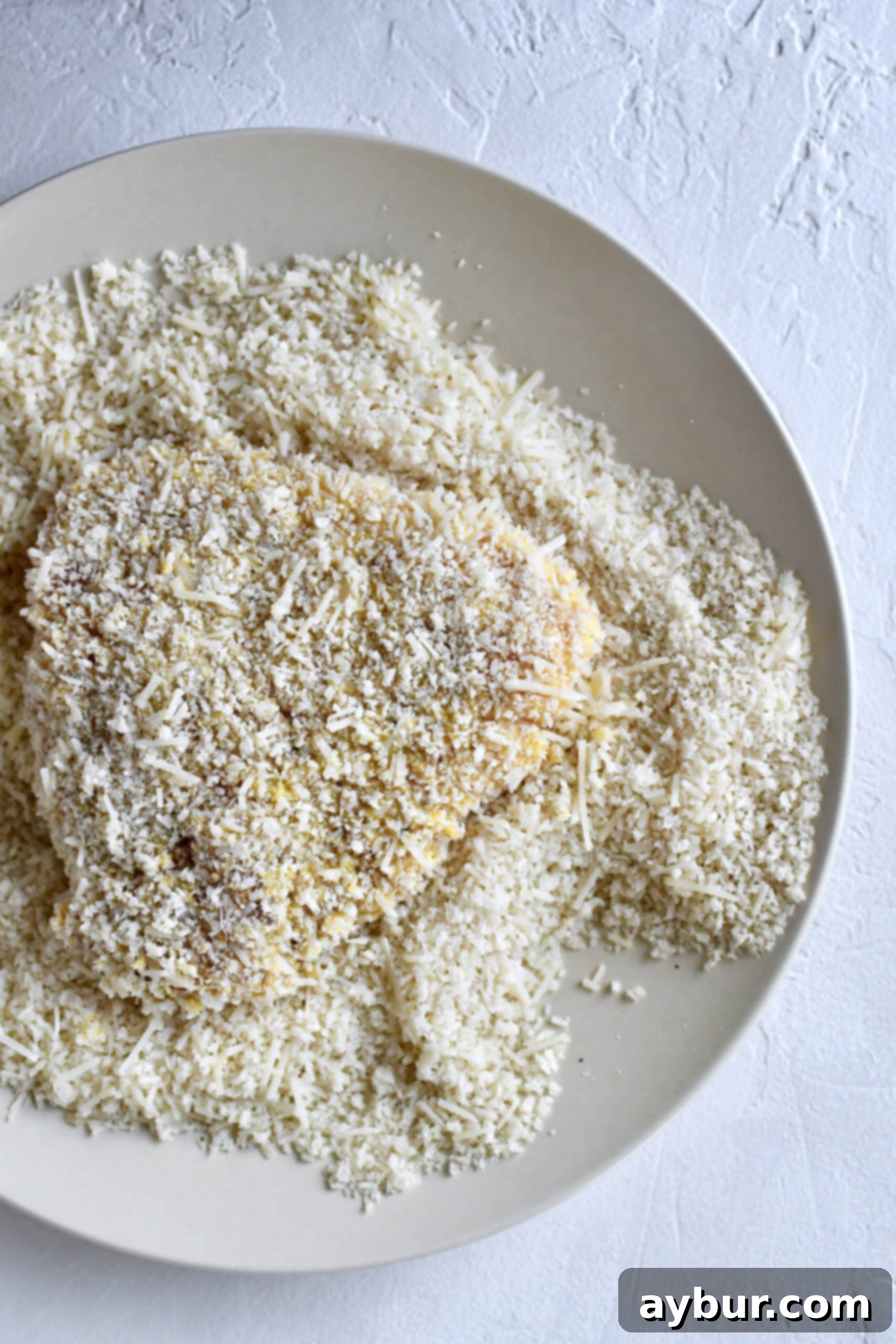 Chicken breast being crusted in parmesan and bread crumbs for a crispy coating.