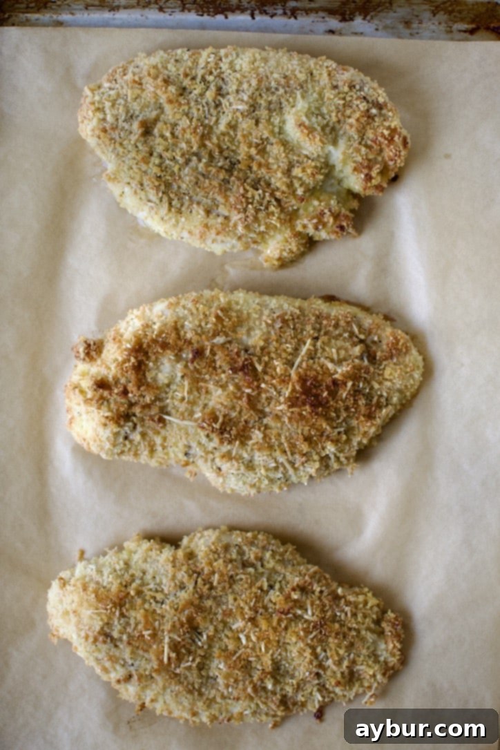 Breaded chicken breasts baking on a parchment-lined sheet.