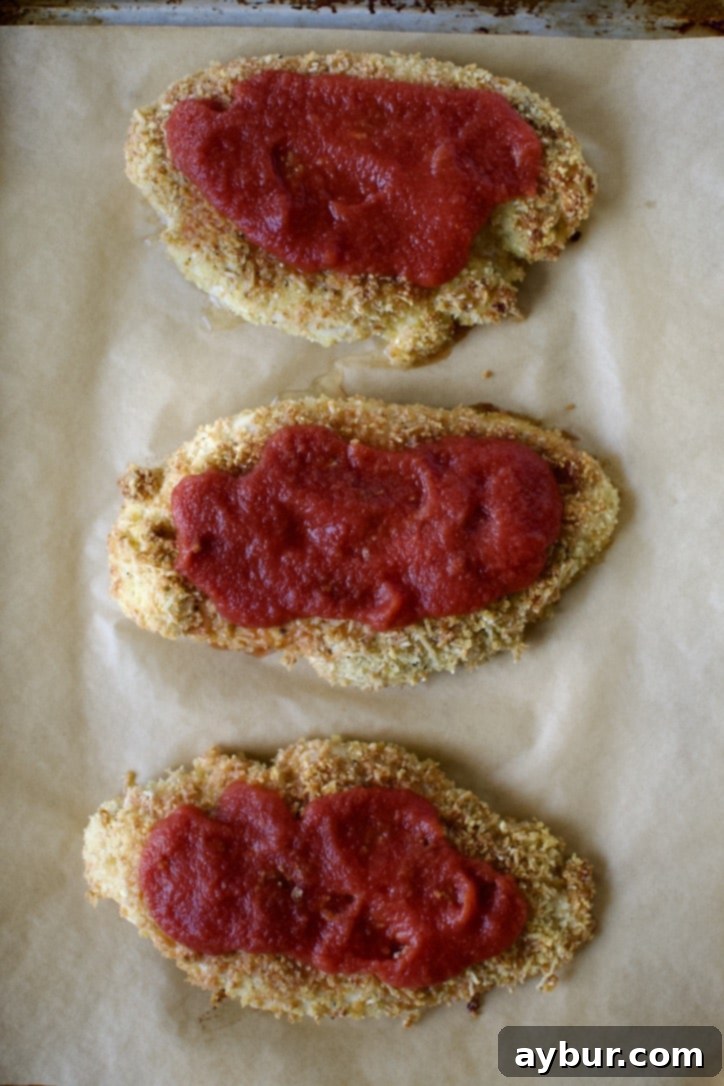 Baked chicken topped with tomato sauce, ready for mozzarella.