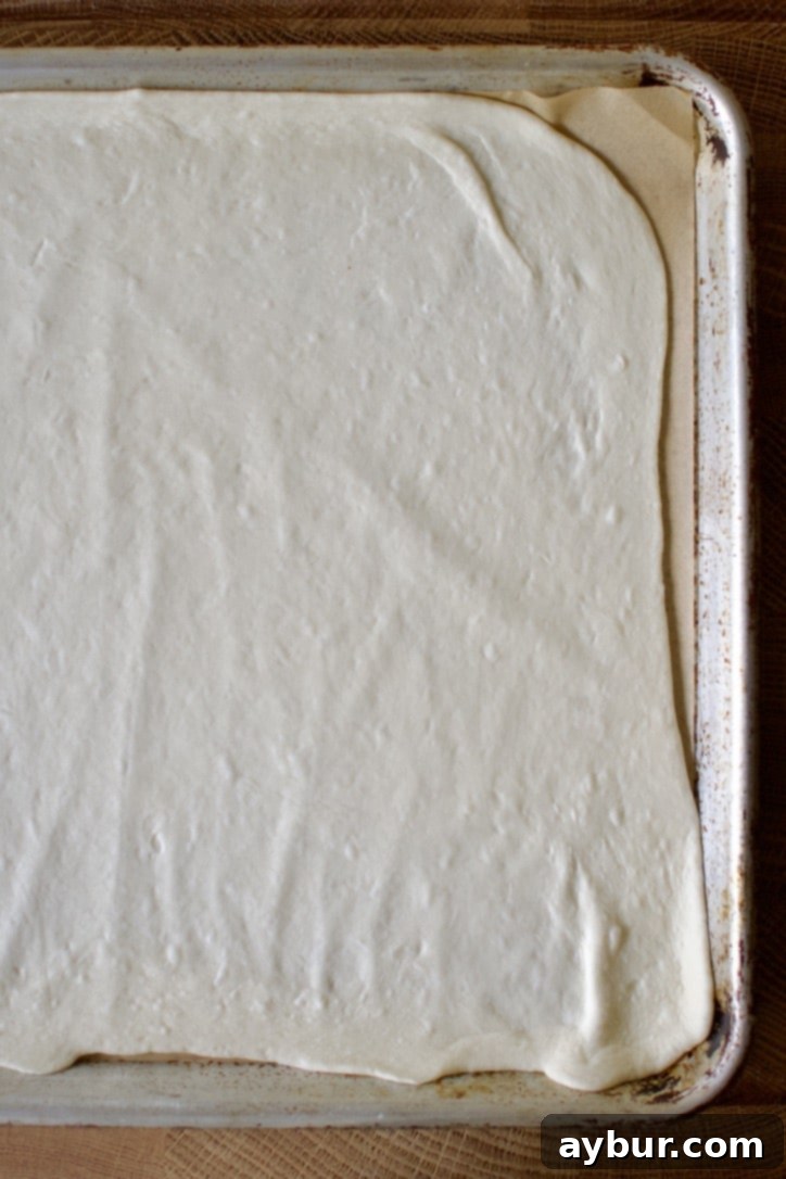 Pizza dough expertly rolled out to the exact dimensions of a sheet pan, awaiting its initial high-heat bake for a crispy finish.