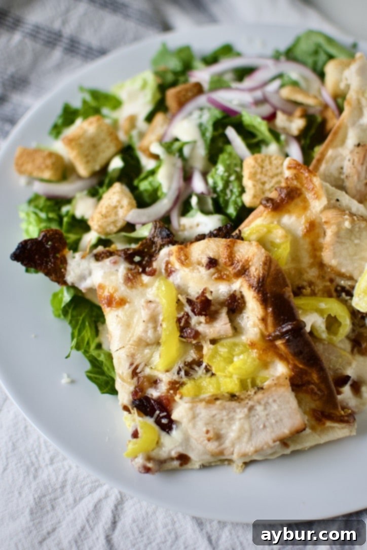 Creamy Garlic White Pizza 12 Two slices of homemade white pizza served on a white plate with a fresh green salad on the side.