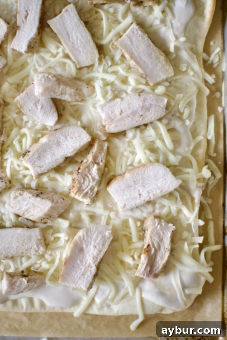 Topping the pizza, sauce, mozzarella, and chicken added.