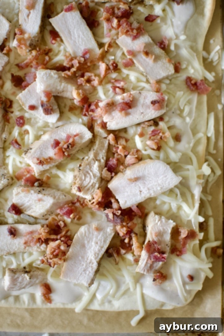 Topping the pizza, sauce, mozzarella, chicken, bacon, and banana peppers added.