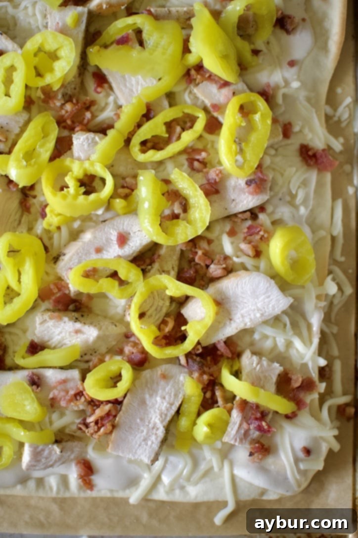 Topping the pizza, sauce, mozzarella, chicken, bacon, banana peppers, and shredded parmesan added.