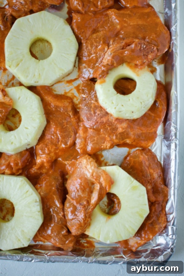 Authentic Al Pastor Tacos 5 Marinated pork and sliced pineapple arranged on a sheet pan, ready for roasting under the broiler.