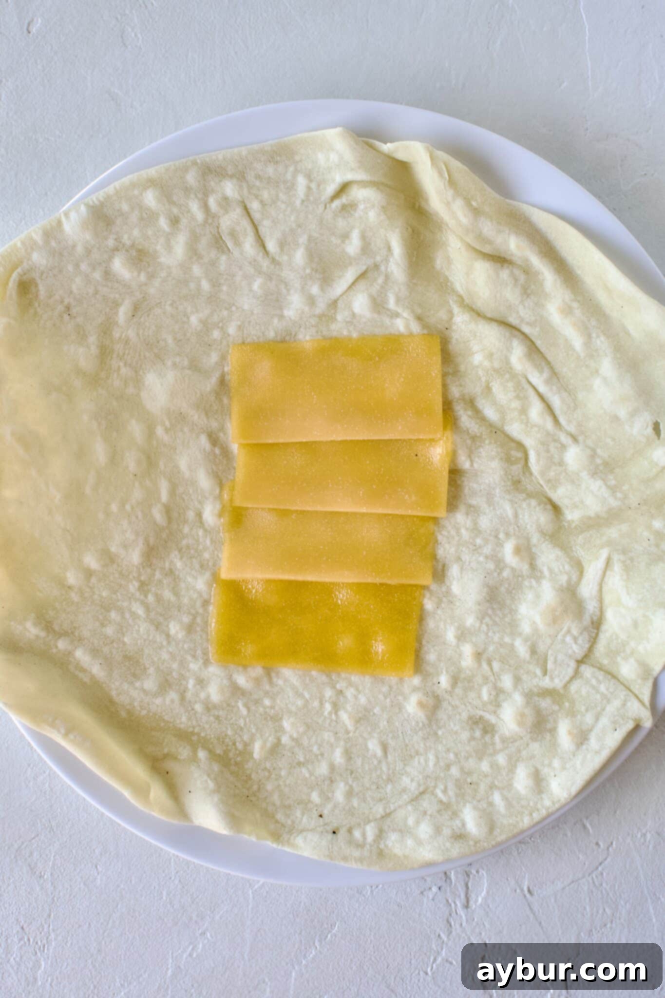 Making a breakfast burrito, cheese added to a warm tortilla.