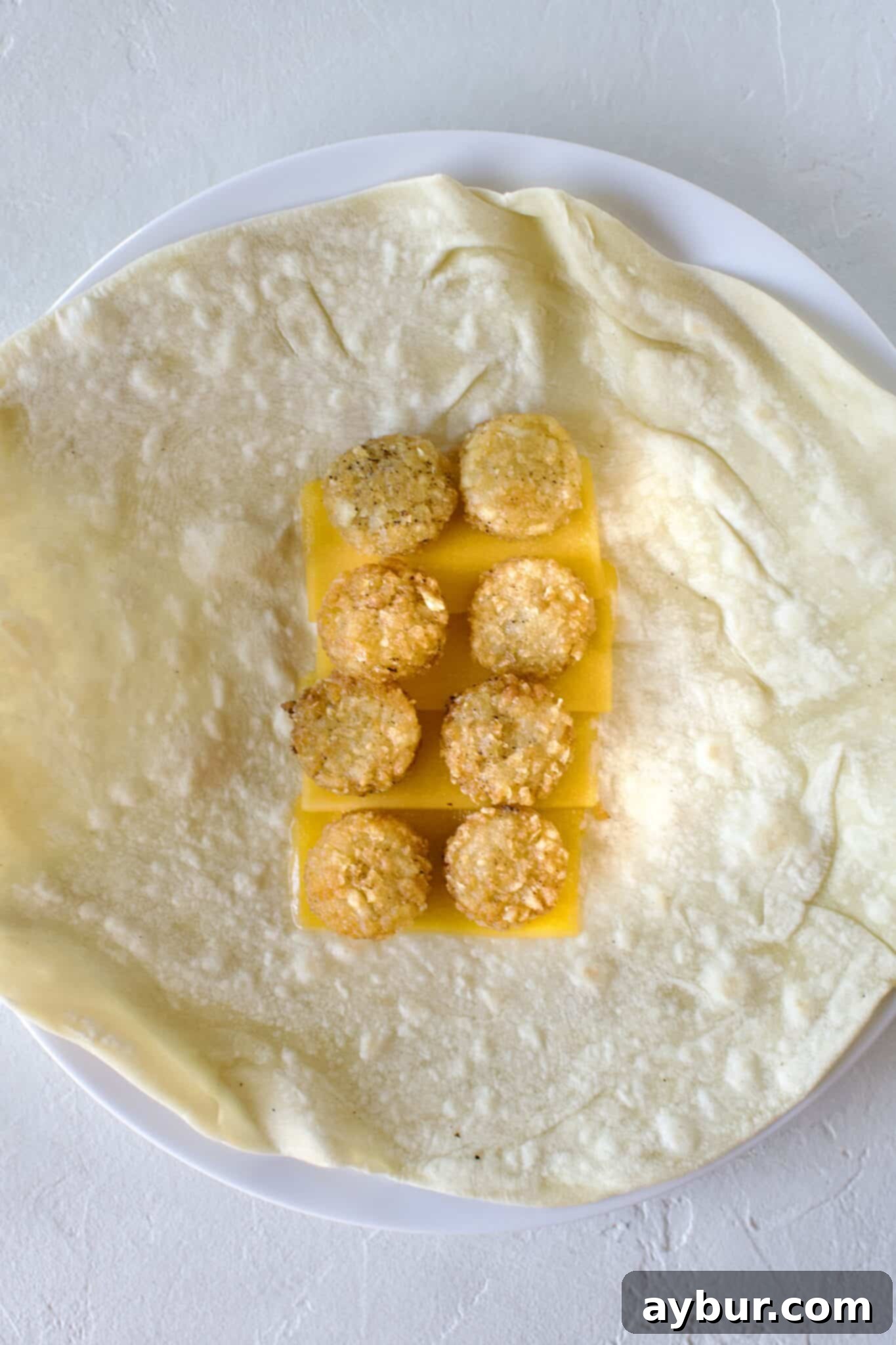 Making a breakfast burrito, cheese, and hash browns added to a warm tortilla.