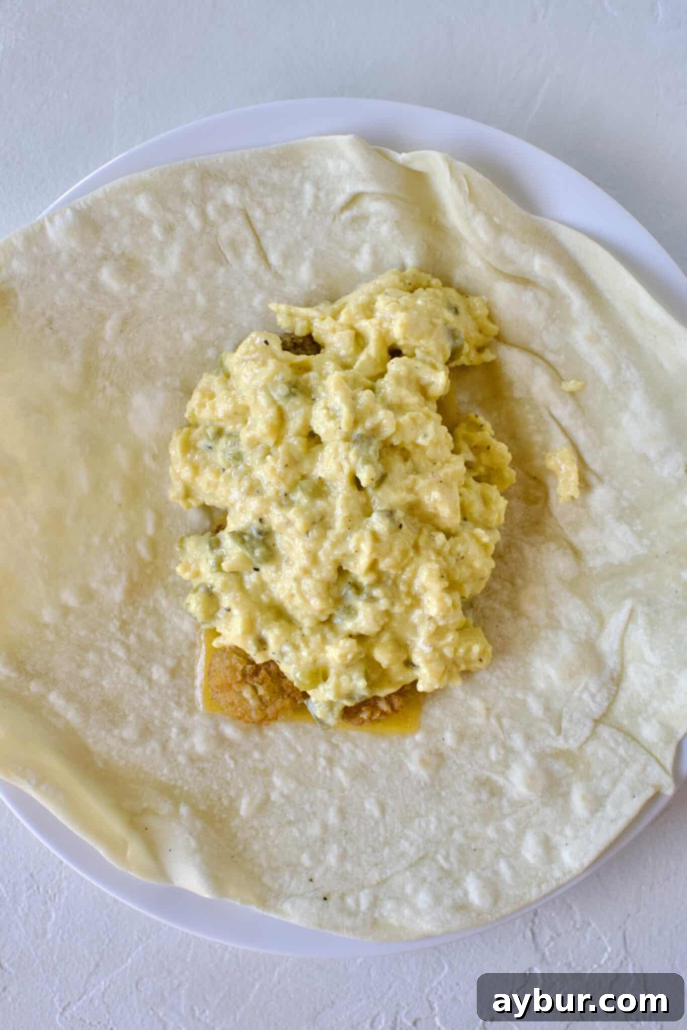 Making a breakfast burrito, cheese, hash browns, and eggs added to a warm tortilla.