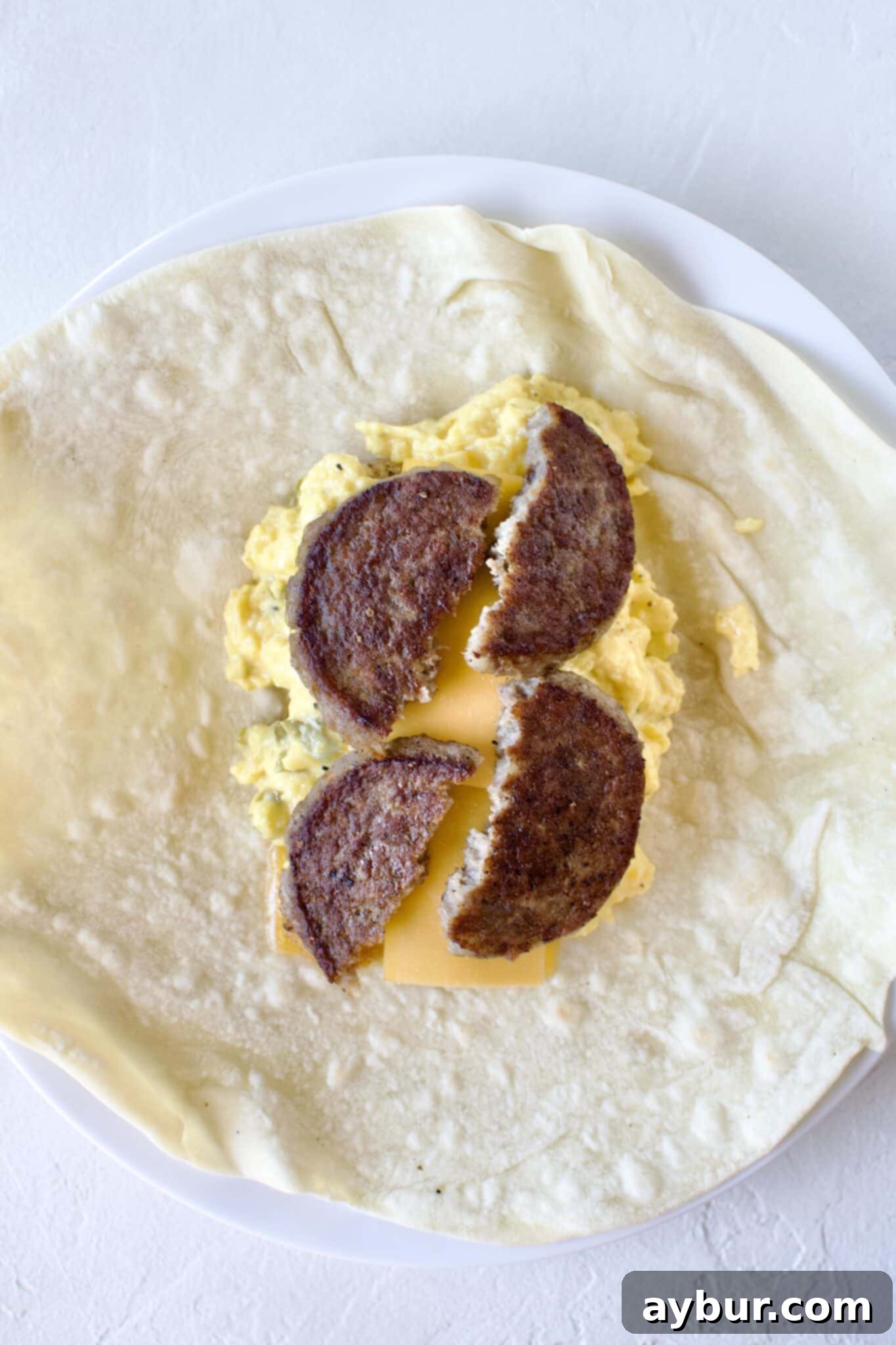Making a breakfast burrito, cheese, hash browns, eggs, and sausage added to a warm tortilla.