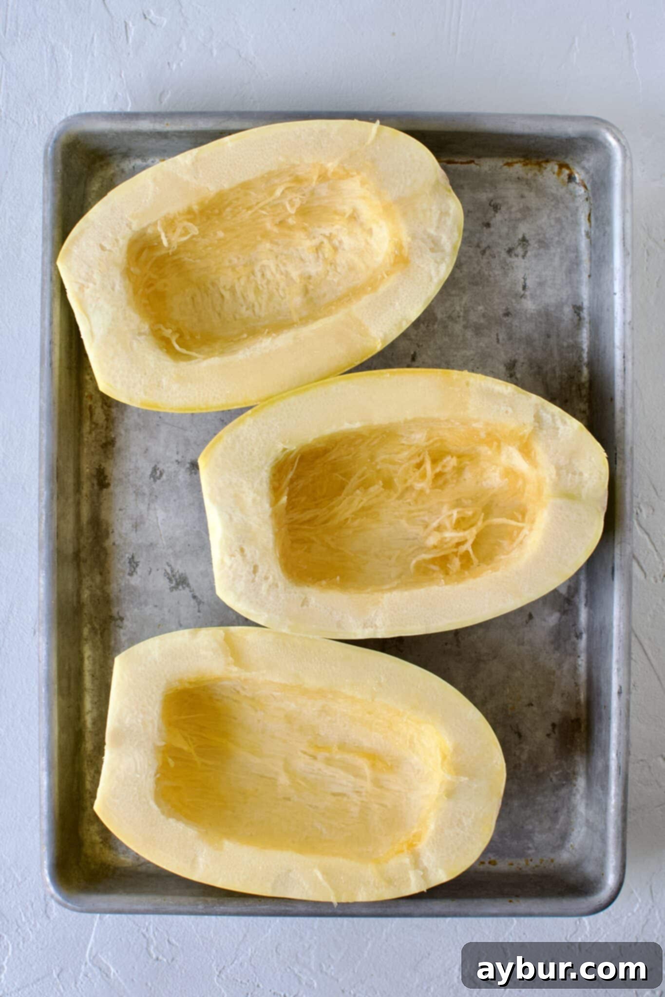 Spaghetti squash halves, with seeds removed, neatly arranged on a baking sheet, ready for seasoning.