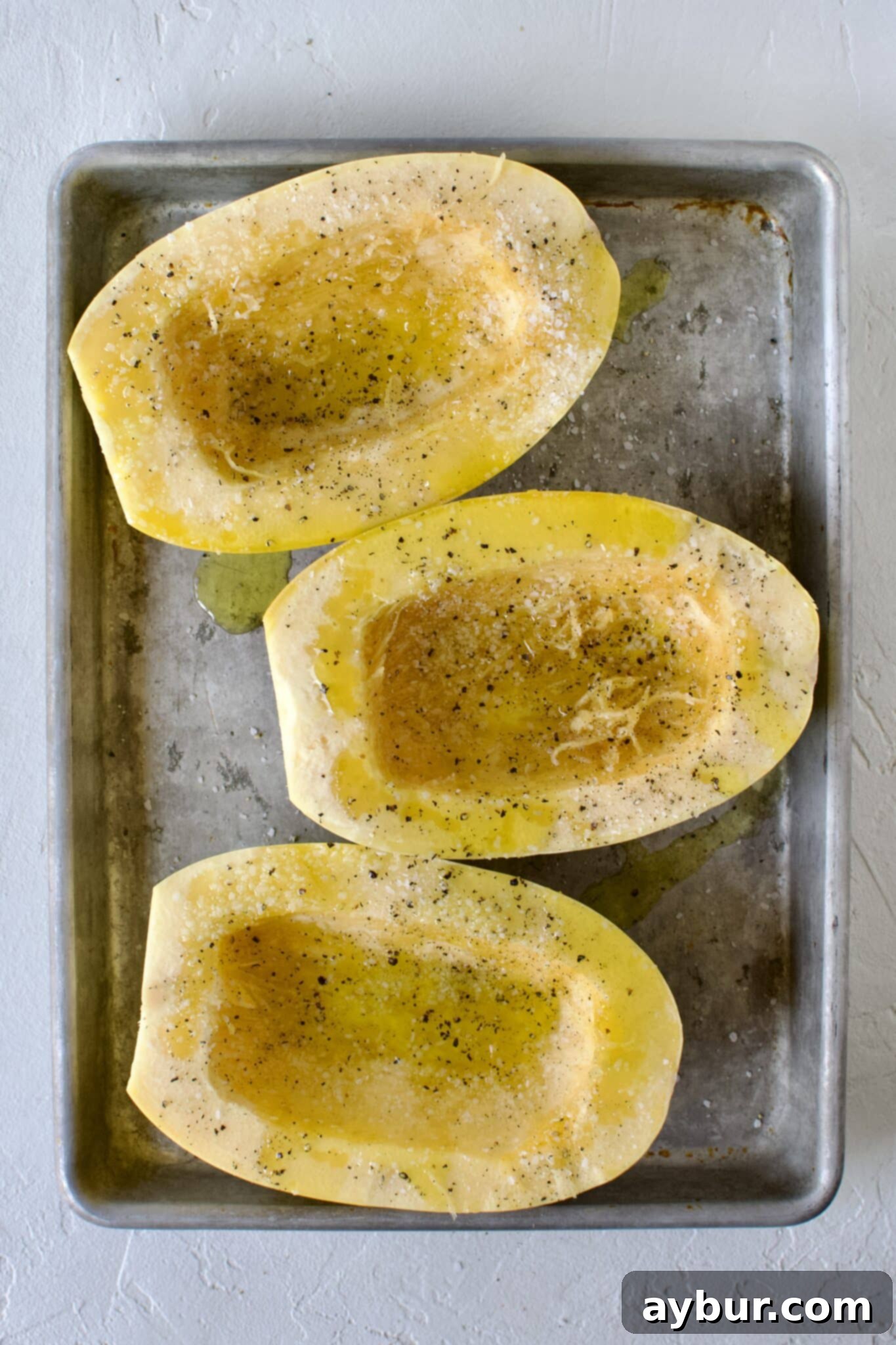 Spaghetti squash halves, cut side up, generously seasoned with olive oil, salt, and pepper on a baking sheet.