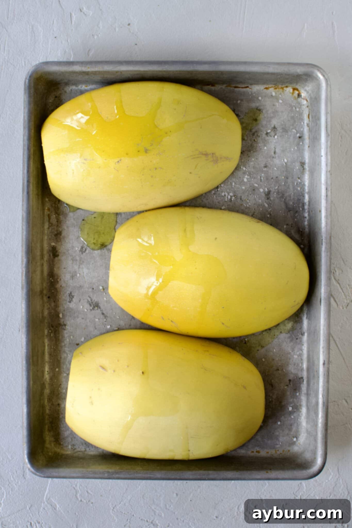 Spaghetti squash halves, seasoned and flipped cut side down on a baking sheet, prepped for roasting.