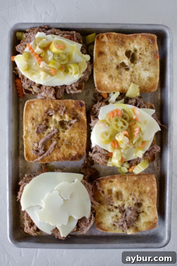 Assembled Italian Beef Sandwiches on toasted ciabatta rolls, topped with melted provolone cheese and giardiniera.