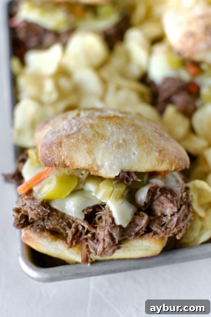 A stunning close-up of an Italian Beef Sandwich, showcasing the tender beef, melted cheese, and fresh giardiniera, served on a platter with chips.