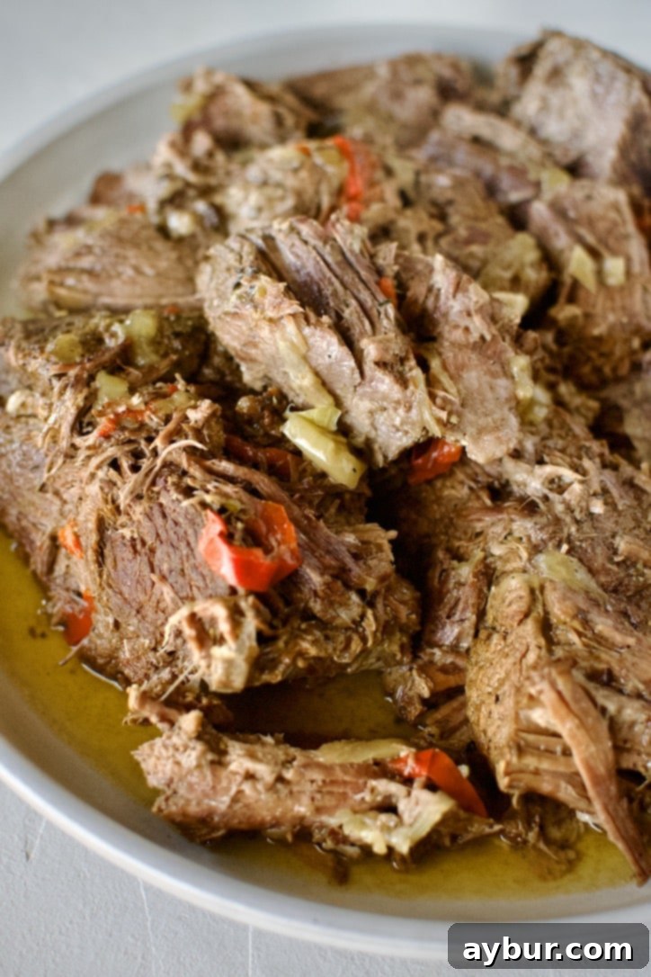 Perfectly stewed beef chuck roast in a pot with onions, bell peppers, seasonings and pepperoncini after stewing 5 hours, ready for shredding.