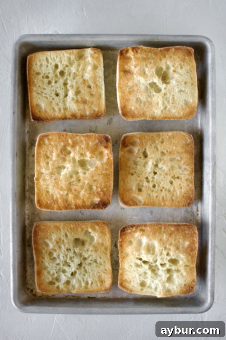 Toasted and opened ciabatta rolls on a sheet tray, showing a golden-brown crispness.