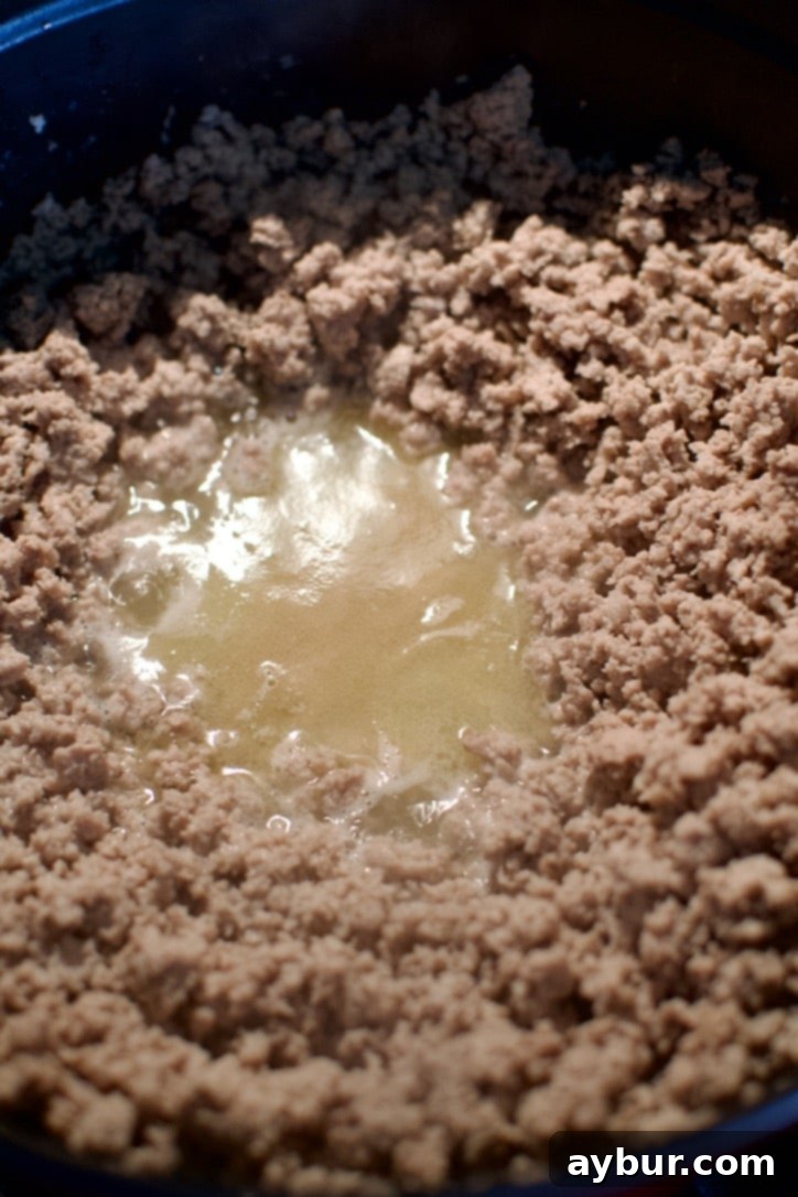 Close-up of browned ground turkey in a large pot before draining excess liquid.