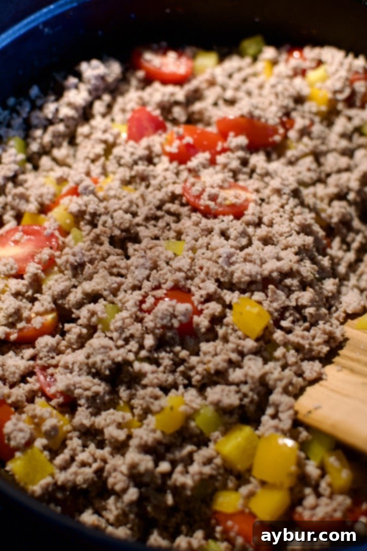 Chopped vegetables, including bell peppers and grape tomatoes, added to the browned ground turkey in the pot, ready to cook.