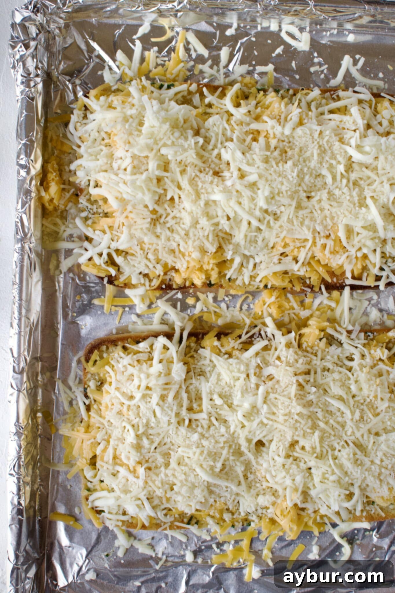 Adding a generous amount of cheese to the toasted garlic bread.