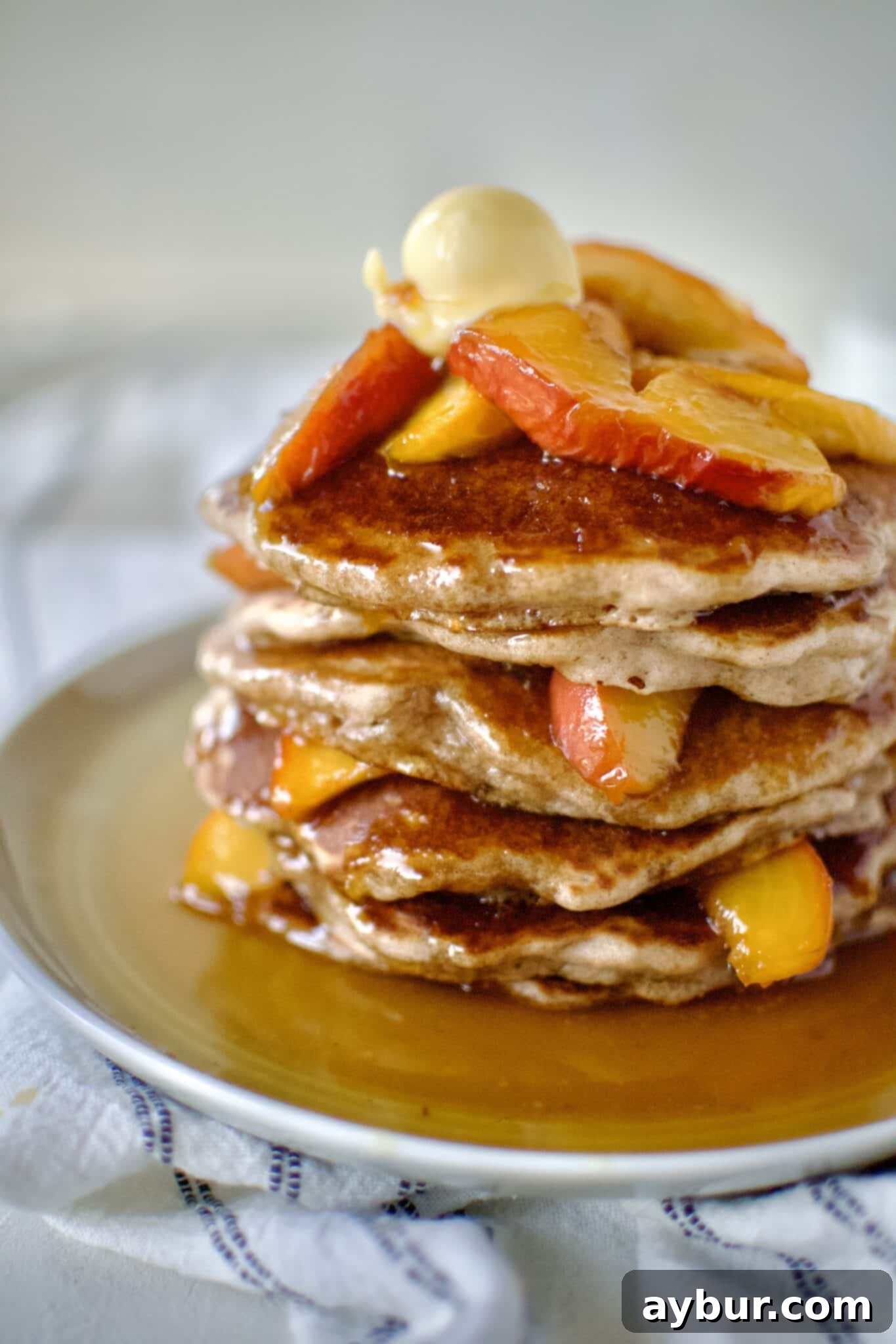 Golden Peach Pancakes 2 A stack of golden brown fluffy Peach Pancakes on a white plate, generously drizzled with a rich whiskey maple peach topping.