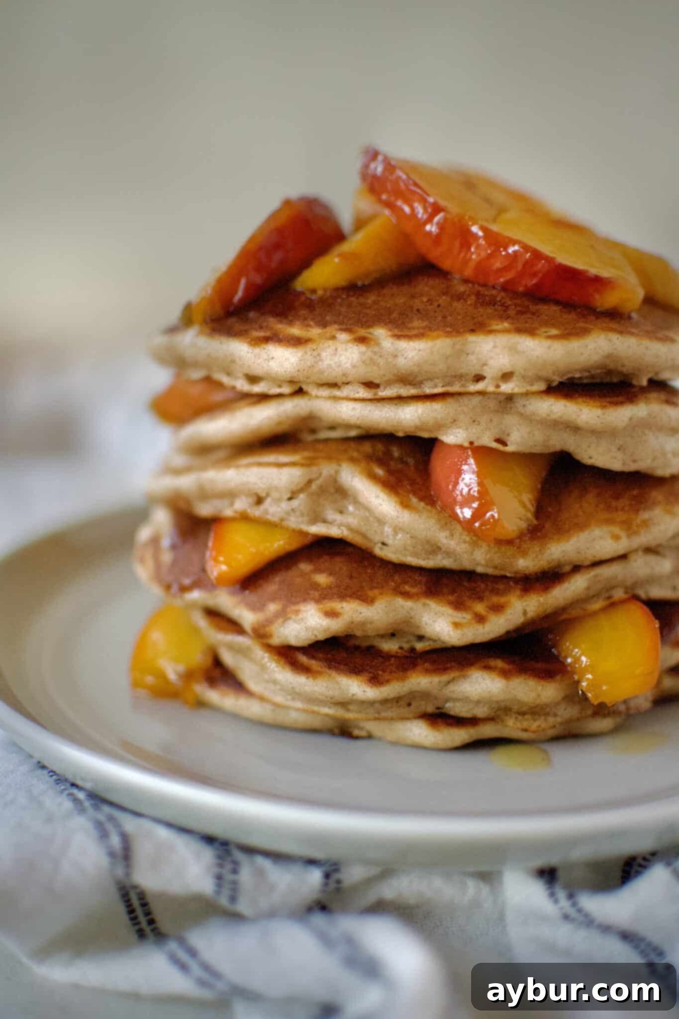Golden Peach Pancakes 12 A close-up shot of a stack of Fluffy Peach Pancakes, glistening with whiskey maple topping and topped with fresh peach slices, ready to be enjoyed.