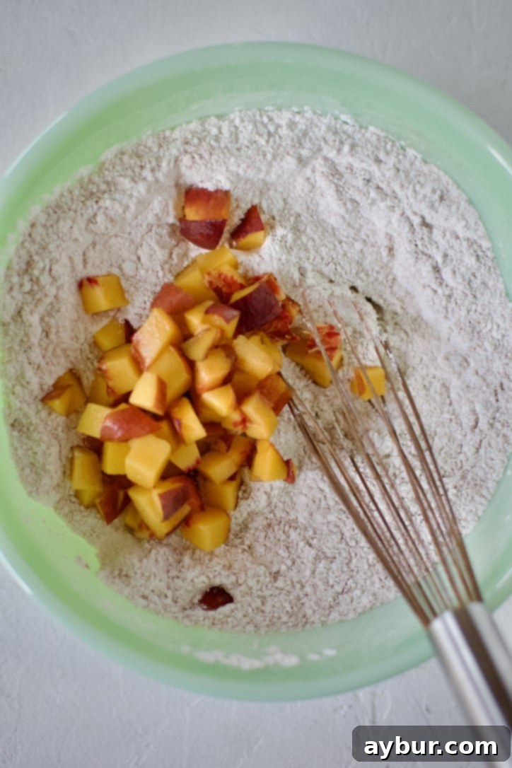 Golden Peach Pancakes 4 Diced fresh peaches being gently folded into a bowl of dry pancake mix ingredients, ready for wet ingredients.