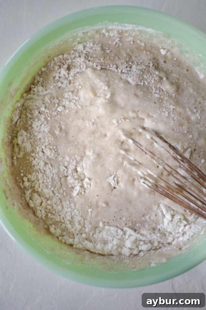 Golden Peach Pancakes 5 Wet ingredients, including milk and melted butter, being whisked into the pancake batter, creating a smooth consistency.