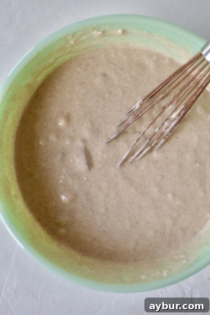 Golden Peach Pancakes 7 A bowl of peach pancake batter, visibly textured and flecked with peach pieces, resting before cooking, indicating proper preparation.