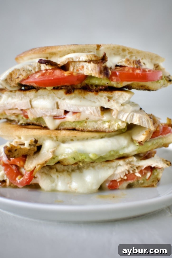Perfectly grilled Pesto Chicken Panini, sliced diagonally and stacked on a white plate, showcasing melted cheese and vibrant fillings, ready to be enjoyed.