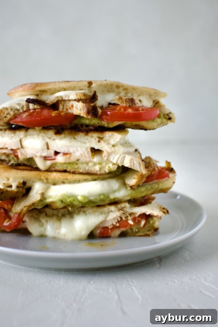 A close-up shot of a halved Pesto Chicken Panini, featuring the appetizing layers of grilled chicken, melted cheese, and fresh tomatoes, perfectly stacked on a wooden cutting board.
