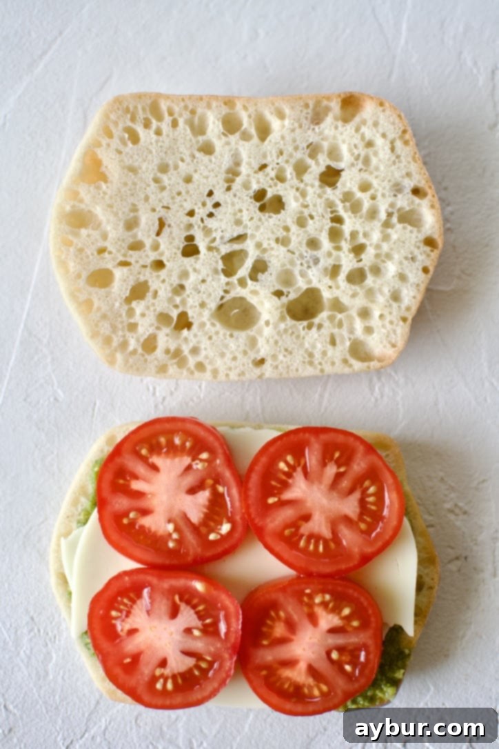 Step 3: Incorporating fresh vegetables. The panini base with pesto and provolone, now adorned with thin slices of juicy red Campari tomatoes.