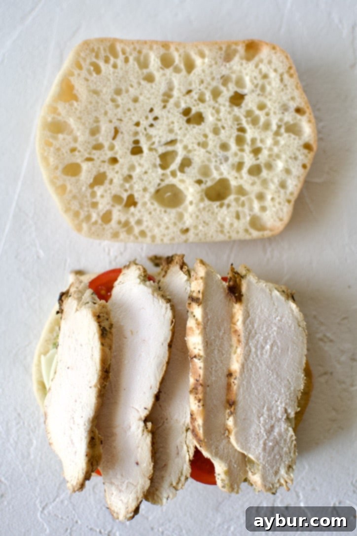 Step 4: Adding the protein. The panini with pesto, provolone, and tomatoes, now layered with tender, thinly sliced cooked chicken breast.