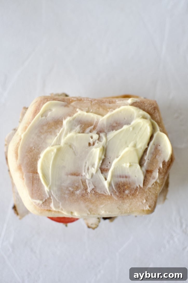 Step 6: Buttering the bread for grilling. The bottom half of the assembled panini, with all its delicious fillings, is generously buttered on its exterior, preparing it for the panini press.