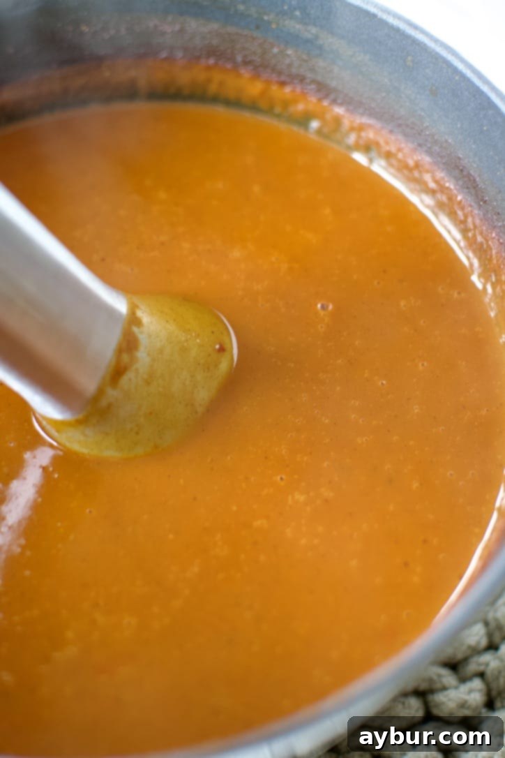 Homemade Red Enchilada Sauce 8 The simmering sauce is being pureed directly in the pot using a hand blender, transforming it into a smooth, consistent red enchilada sauce.