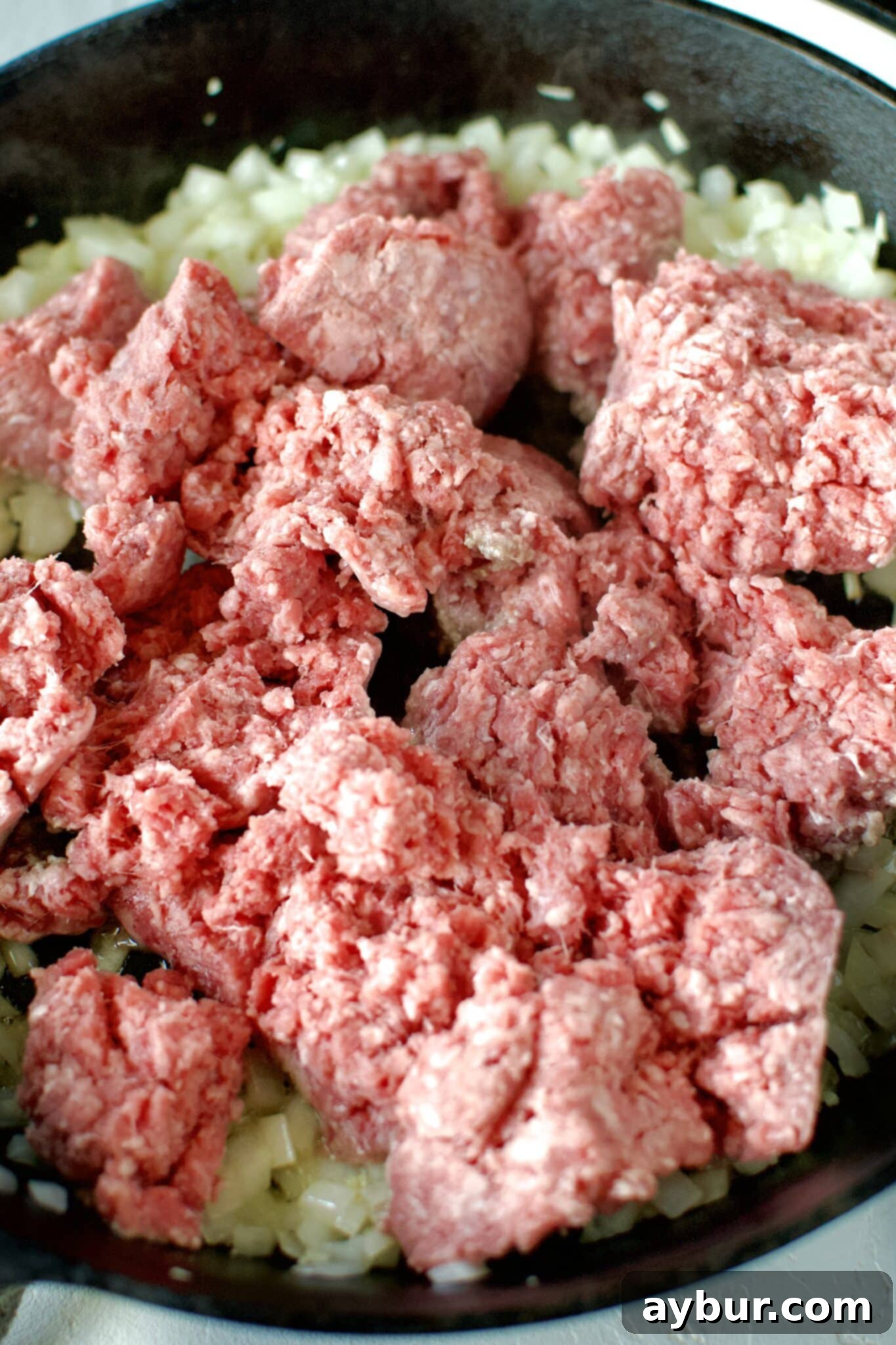 Adding the ground beef to sautéed onions and garlic in a cast iron skillet.