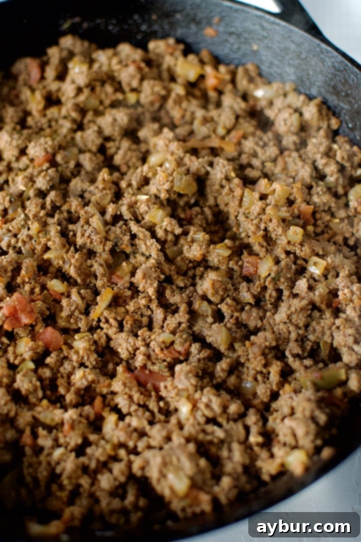 Fully cooked and seasoned ground beef, ready to be mixed with cheese for the enchilada filling, shown in a cast iron skillet.