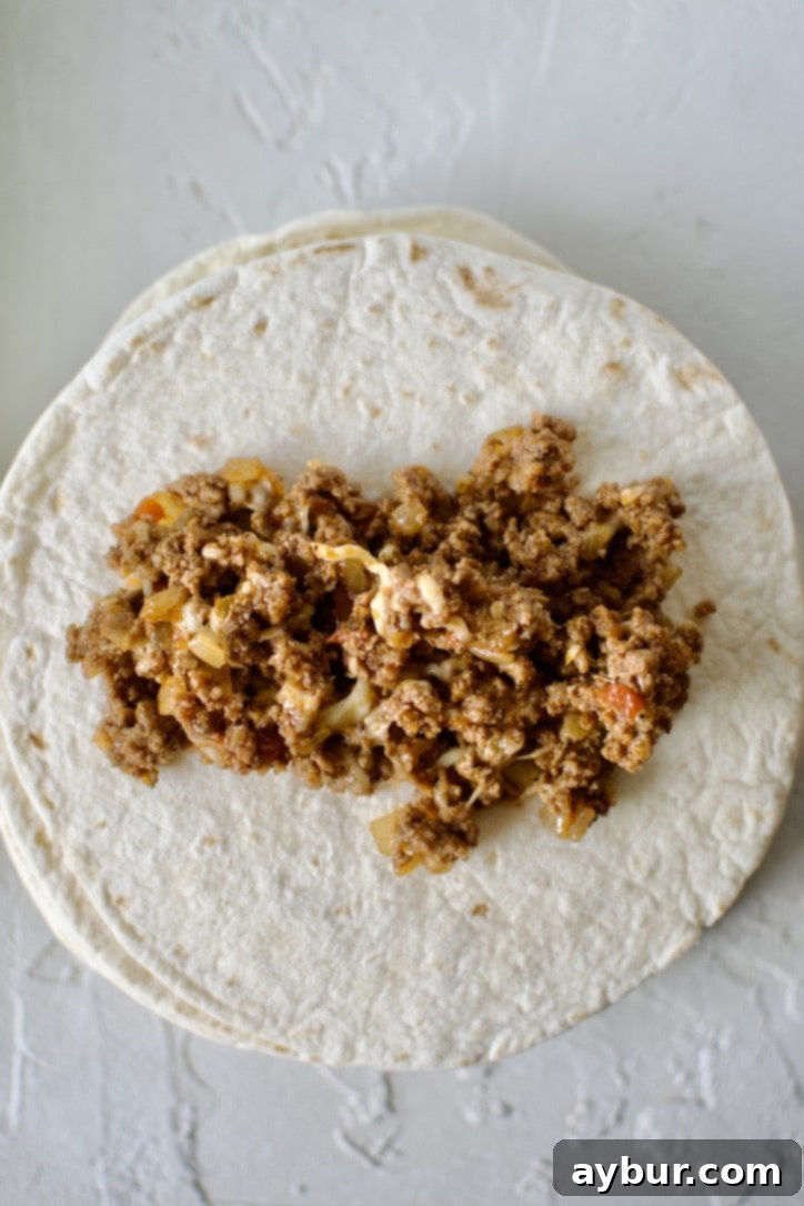 Carefully filling a flour tortilla with the ground beef and cheese enchilada filling.
